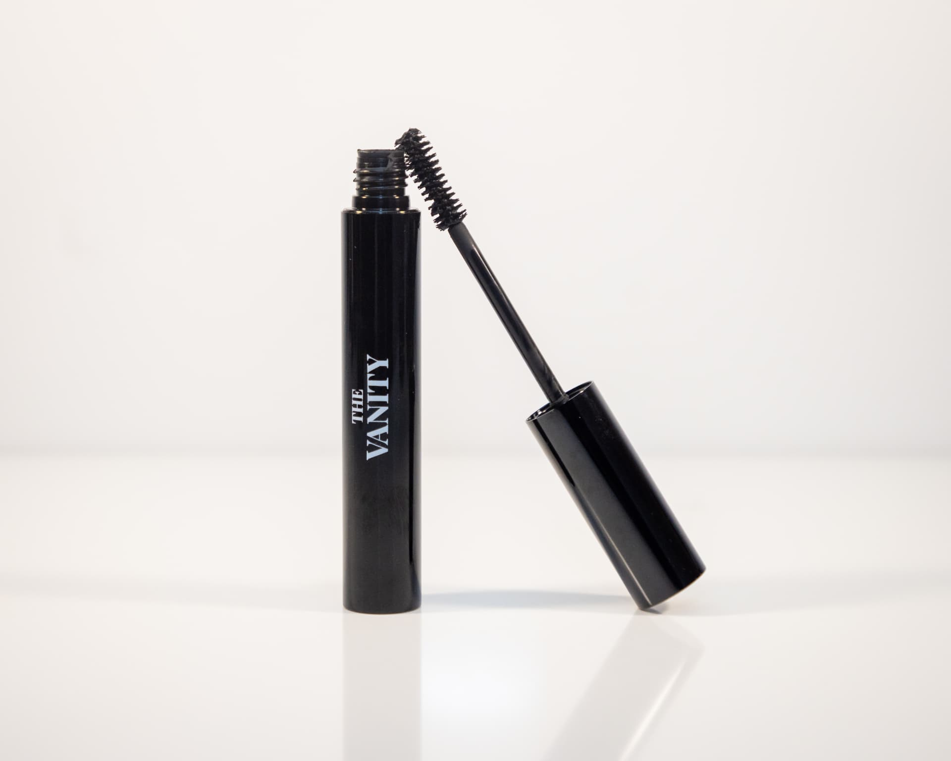 The Vanity black mascara tube with wand leaning against it on white
