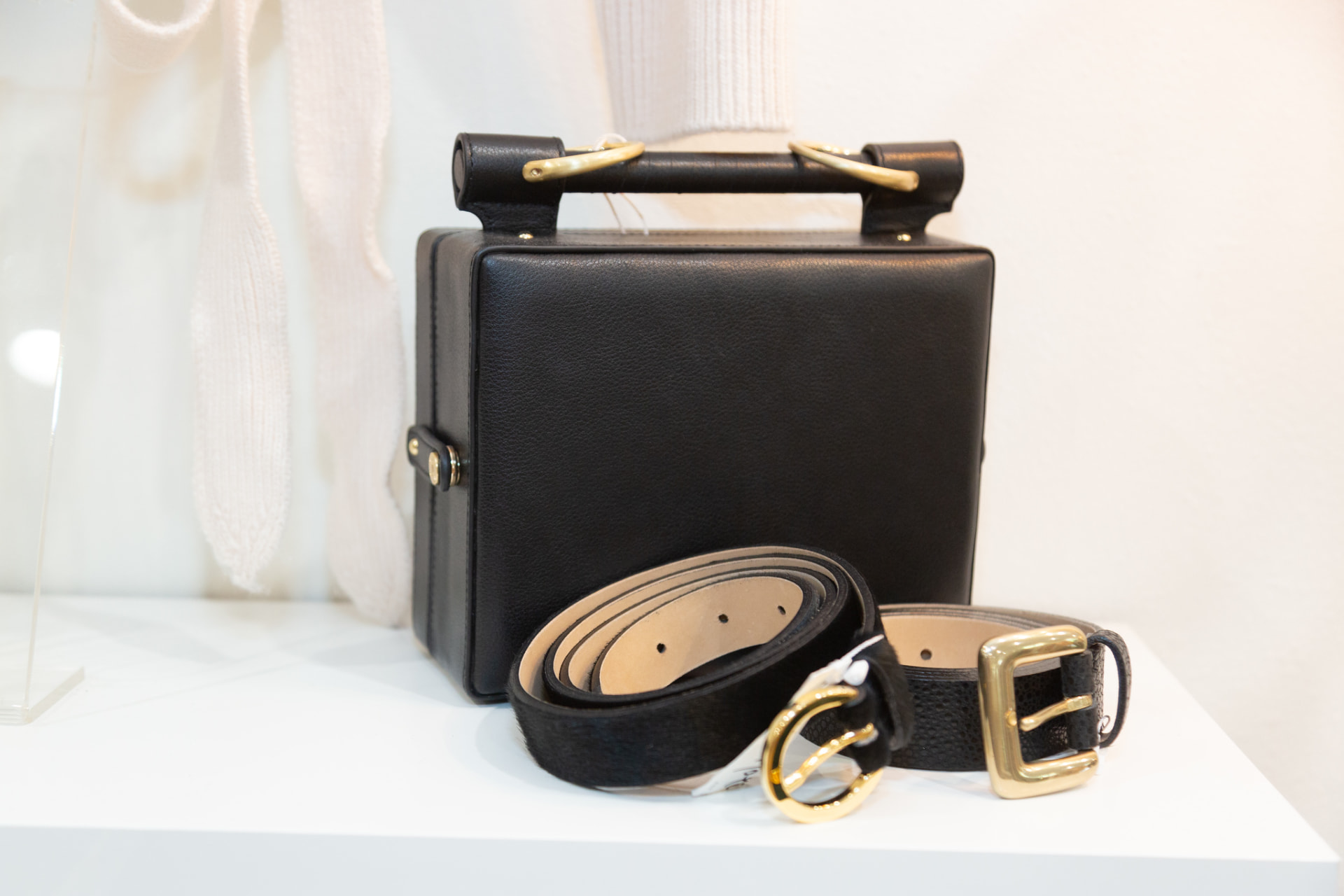 Black leather box bag with gold buckle belts on a retail shelf