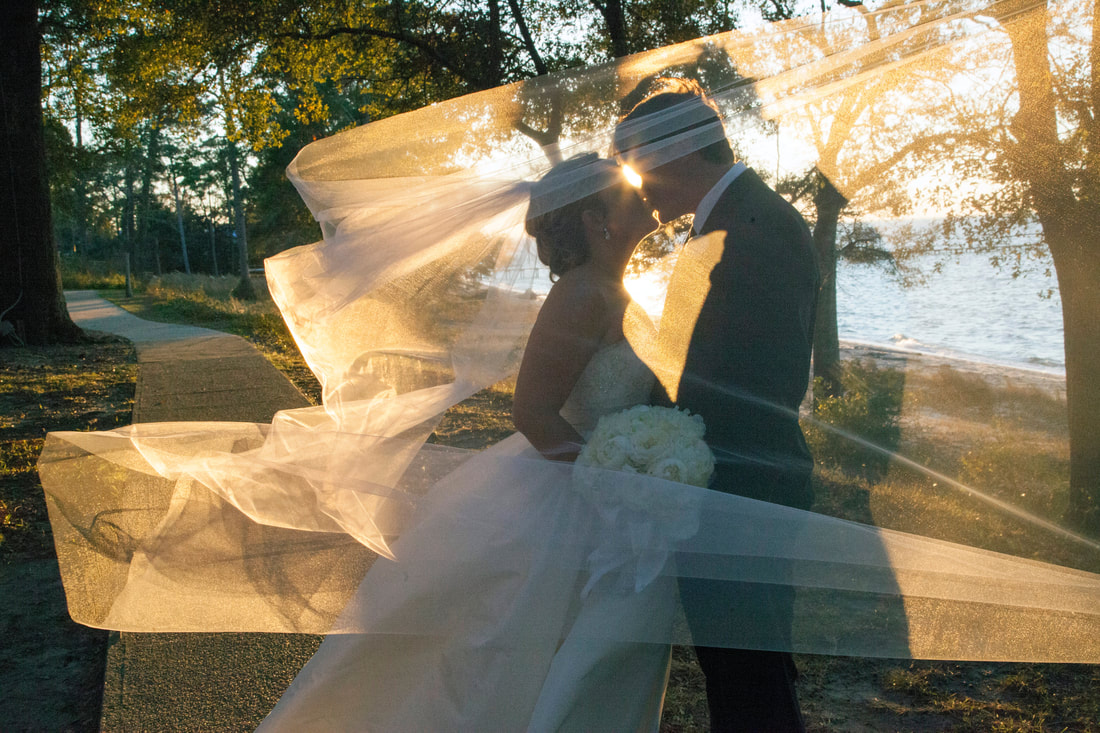 Bride and groom kissing as the veil catches the sunset by the water