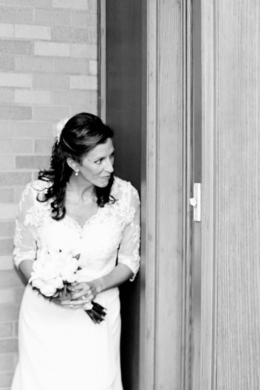 Black and white portrait of the bride waiting in a doorway with her bouquet
