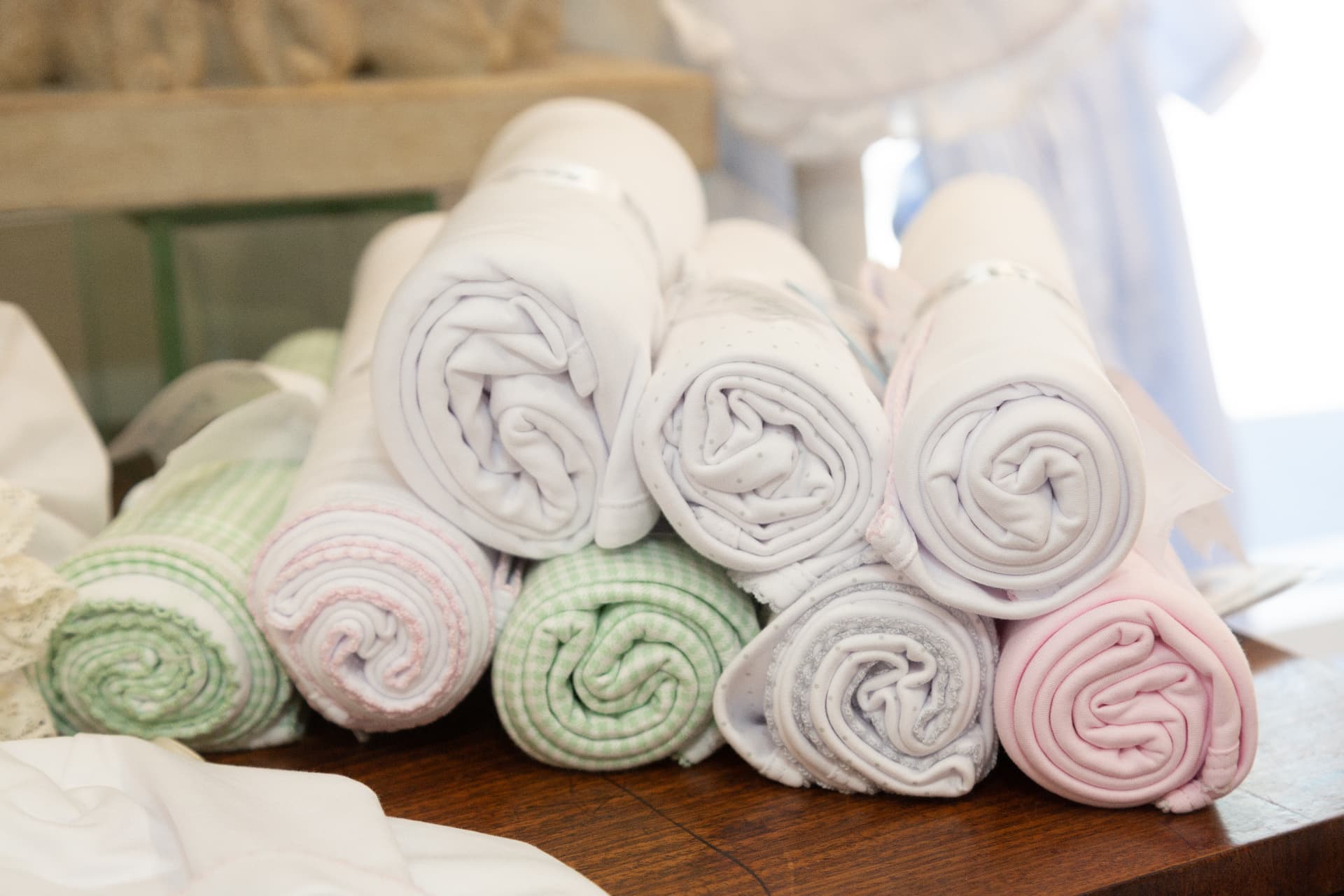 Rolled pastel baby blankets stacked on a wooden table