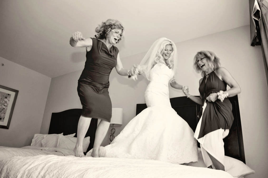 Black and white photo of the bride jumping on the bed with family