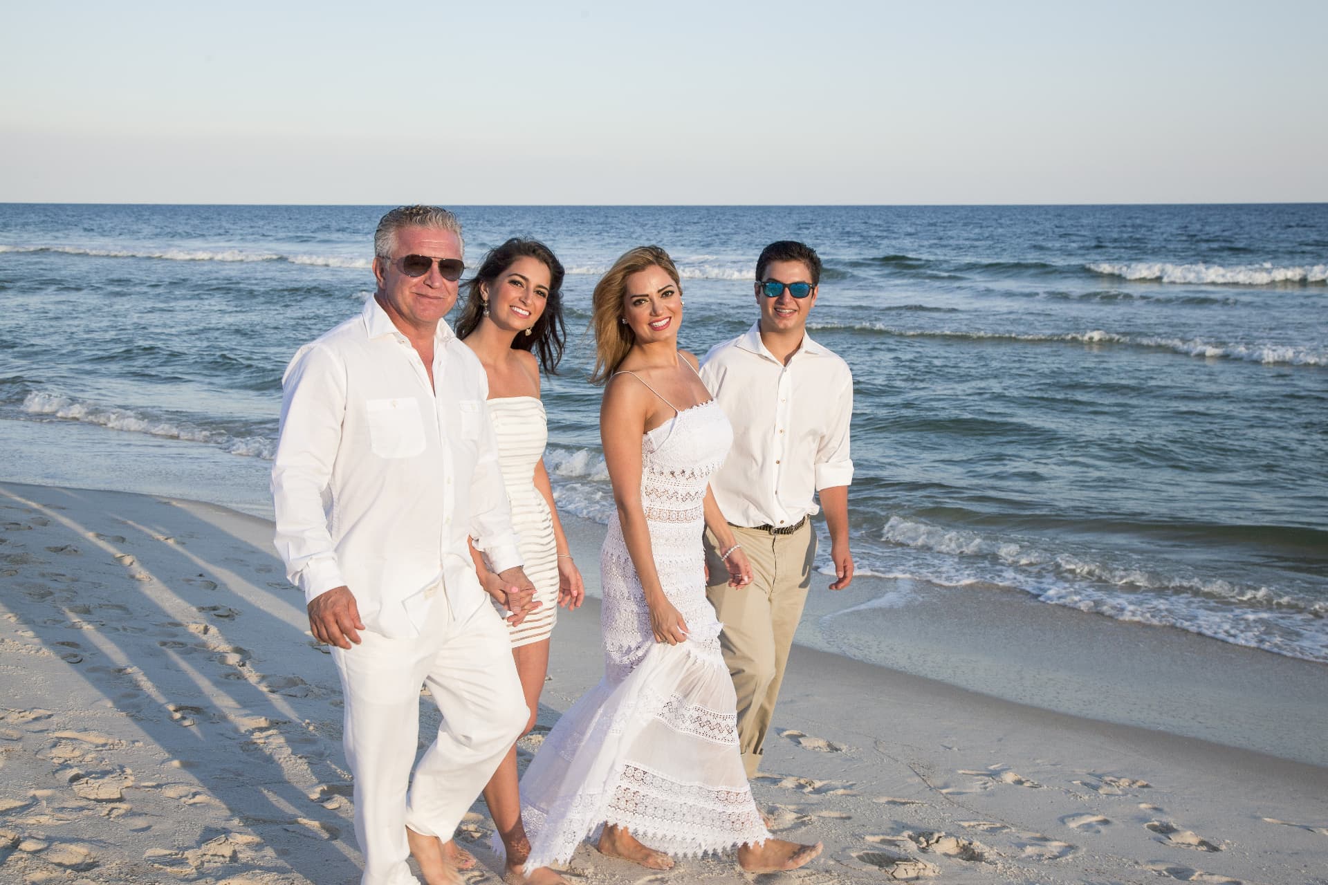 Family in white walking the Gulf shoreline at sunset