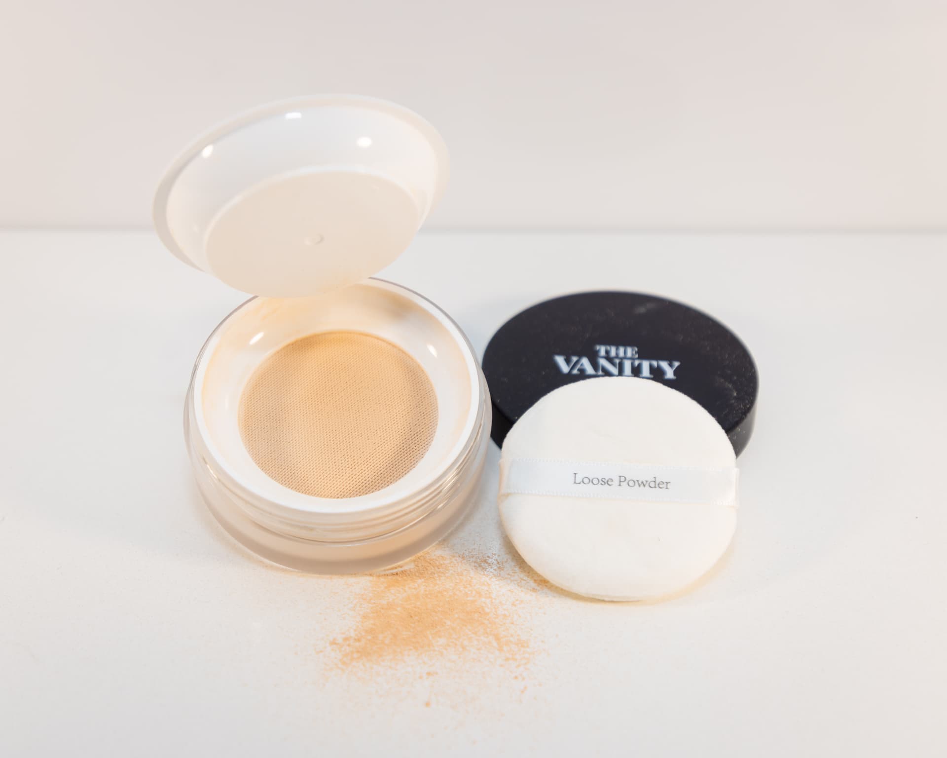 The Vanity loose powder jar open with puff, powder dusted across the surface