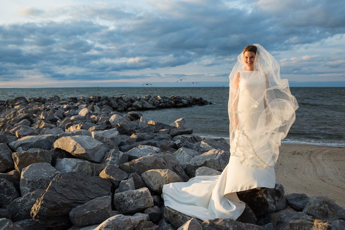 Bride with her veil blowing across the rocks at sunset