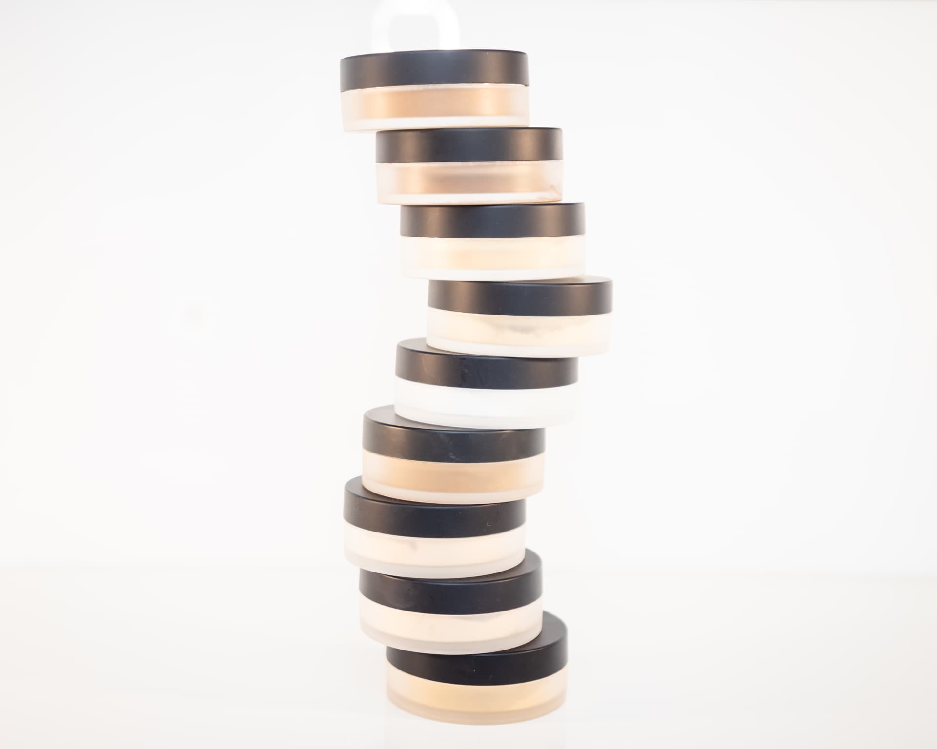 Tall stack of The Vanity loose powder jars balanced on a white background