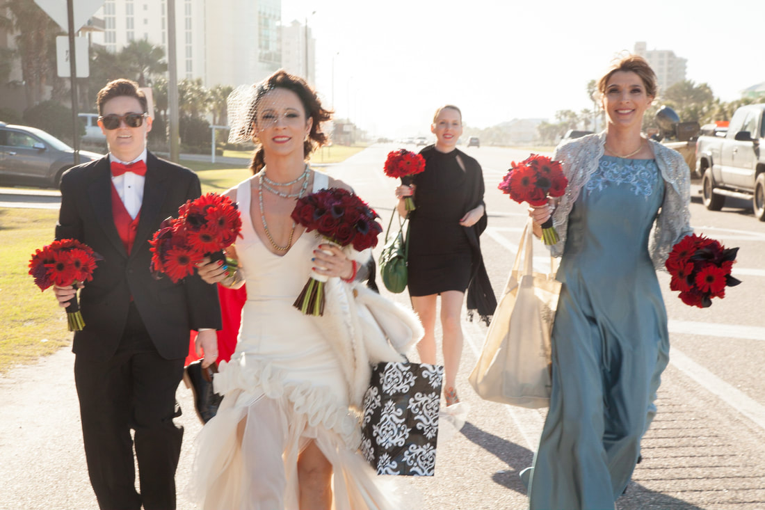 Bridal party walking along the beach road with red bouquets