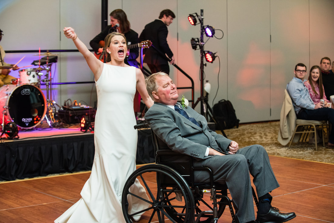 Bride cheering while dancing with her father in a wheelchair